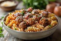 Homemade fusilli pasta with juicy meatballs in rich tomato sauce, garnished with fresh herbs and parmesan cheese, served in gray ceramic bowl on wooden table.