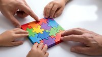 Diverse hands collaborating to assemble colorful rainbow puzzle pieces on white surface, representing teamwork, problem-solving and unity in business.