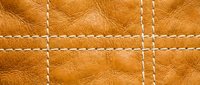 Brown leather texture with white decorative stitching in grid pattern. Natural grain surface with contrasting thread details for fashion and craft projects.