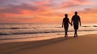 Romantic couple silhouettes walking hand in hand on beach at sunset with orange pink sky reflecting on ocean waves creating peaceful evening atmosphere.