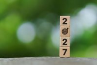 Wooden blocks displaying 2027 with target symbol stacked vertically against blurred green bokeh background representing business goals and future planning.