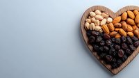 Heart-shaped wooden plate filled with dried blueberries, raw almonds and pistachios on light background. Healthy snack concept for Valentine's day.