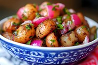 Fresh baby potatoes with pink pickled onions and herbs served in traditional blue and white ceramic bowl, close up view of homemade side dish.