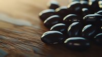 Fresh black beans scattered on rustic wooden surface with dramatic lighting and shallow depth of field, macro food photography for culinary projects.