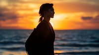 Silhouette of Asian woman with ponytail against dramatic orange sunset sky and ocean waves, side profile capturing contemplative peaceful moment at beach during golden hour.