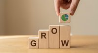 Hand placing wooden block with pie chart icon to complete GROW word on staircase arrangement, symbolizing business growth and success.