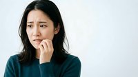 Young Asian woman with long dark hair wearing teal sweater, hand near mouth, expressing worry, stress, or concern. Isolated on white background for design use.