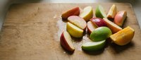 Fresh colorful apple slices arranged on rustic wooden cutting board for healthy snacking and cooking preparation.