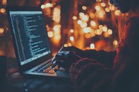 Programmer working late at night on laptop with code visible on screen, atmospheric bokeh lights in background creating cozy ambient environment.