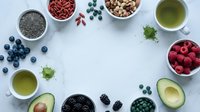 Superfood ingredients arranged in circle on white background with green tea, berries, nuts, seeds and avocado for healthy nutrition and wellness lifestyle.