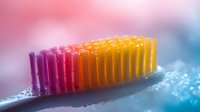 Colorful toothbrush bristles in pink, purple and orange gradient macro photography with water drops and soft bokeh background for dental hygiene concept.