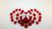 Red rose petals arranged in heart shape with white ribbon bow on light background for romantic Valentine's Day celebration and love concept.
