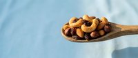 Mixed nuts and dried fruits on wooden spoon against blue background. Healthy snacking, organic food ingredients for cooking and baking recipes.