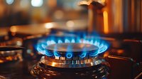 Blue flame from gas stove burner in kitchen, close up view with bokeh background showing natural gas combustion on modern cooktop appliance.