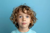 Young Caucasian boy with bright blue eyes and curly blonde hair looking up with wonder against turquoise background, wearing matching blue t-shirt, expressing curiosity.