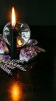 Mystical altar setup with burning black candle, crystal ball, amethyst geodes and dried lavender sprigs creating atmospheric spiritual ambiance for meditation rituals.