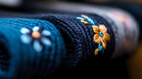 Cozy knitted winter sweater with floral embroidery pattern in blue and orange colors, close-up macro shot showing detailed wool texture and decorative stitching.