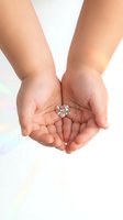 Female hands cupped together holding sparkling heart-shaped diamond jewelry piece against soft white background for romantic gift concepts.