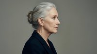 Elegant senior Caucasian businesswoman in profile with gray hair bun wearing black blazer against neutral background for professional corporate branding.