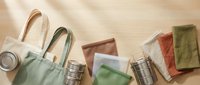 Flat lay composition featuring reusable shopping bags, glass containers, and cloth napkins on neutral background for sustainable lifestyle and eco-friendly living concepts.