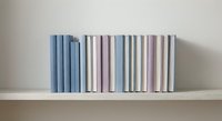 Row of pastel colored books arranged on wooden shelf against neutral wall creating minimalist home decor and organization display for interior design.