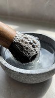 Natural pumice stone with wooden handle brush in stone bowl for exfoliating skincare routine and spa treatments at home.