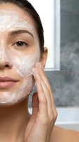 Young woman applying exfoliating face scrub with natural particles in modern bathroom for skincare routine and beauty treatment.