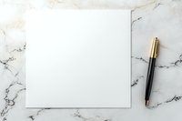 Blank white square paper sheet with luxury gold and black pen on marble background, ready for design mockup or business presentation.