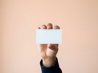 Male hand holding blank white card against neutral beige background. Isolated on solid color for advertising, marketing messages, promotional campaigns, and business communications.
