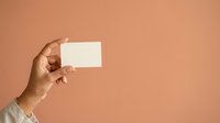 Hand holding blank white card against warm peachy background. Suitable for business branding, marketing campaigns, and promotional material presentations.
