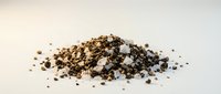 Pile of crushed black peppercorns and coarse ground pepper spice seasoning scattered on white background for culinary cooking and food preparation.