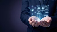 Professional businessman in dark suit holding glowing digital security icons and data analytics interface in cupped hands representing cybersecurity technology.