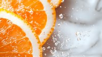 Fresh orange slice with sparkling water bubbles and ice cubes creating refreshing citrus splash for summer beverages and healthy lifestyle concepts.