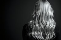 Back view of long wavy platinum blonde hair on dark background, dramatic black and white contrast showing luxurious hairstyle texture and shine.