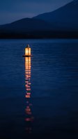 Glowing lantern floating on calm lake water at dusk with mountain silhouettes creating peaceful reflection for meditation and relaxation concepts.