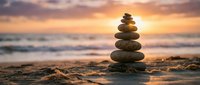 Balanced stone cairn on sandy beach at golden sunset with ocean waves creating peaceful zen meditation atmosphere for wellness and mindfulness practices.