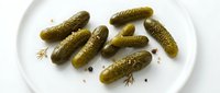 Pickled gherkins and peppercorns arranged on white plate, isolated food ingredient for culinary, recipe, and restaurant design projects.
