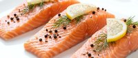 Fresh salmon fillets with lemon slices, dill herbs and black peppercorns on white background. Raw fish portions ready for cooking and healthy meals.