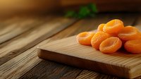 Sweet dried apricots arranged on wooden cutting board against rustic table background with soft natural lighting and shallow depth of field.