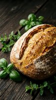 Artisan sourdough bread loaf with golden crust on rustic wooden table surrounded by fresh basil and oregano herbs for culinary and bakery concepts.