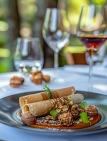 Gourmet dessert plate featuring rolled crepes with caramel sauce, candied nuts and fresh herbs, served with wine selection in elegant restaurant setting.