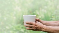 Mature man holding blank white cup with blurred green nature background, suitable for beverage branding, wellness campaigns, and lifestyle marketing materials.