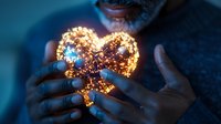 Glowing heart-shaped light decoration held in dark setting creates magical atmosphere with warm golden illumination against blue background. Romantic mood concept.