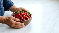 Farmer's hands holding fresh red cherries in cupped palms over white marble surface, showcasing organic produce for agriculture and food industry use.