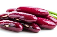 Fresh red kidney beans with water drops on glossy surface, macro shot showing natural texture and vibrant color against white background.