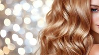 Luxurious blonde wavy hair with soft bokeh lights background. Close up of healthy shiny golden waves styled with professional haircare products for salon advertising.