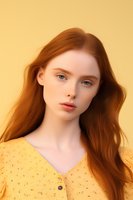 Young woman with flowing red hair wearing yellow polka dot blouse against warm yellow background, natural makeup and soft lighting create romantic spring portrait.