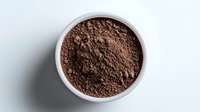 Fine cocoa powder in white ceramic bowl on light background, overhead view showing rich brown color and powdery texture for culinary and baking concepts.