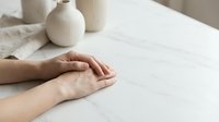 Calm female hands resting on white marble surface with neutral ceramic vases in background, minimal Scandinavian interior style.