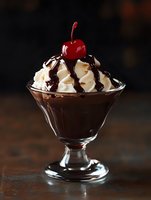 Chocolate ice cream sundae with whipped cream, cherry and syrup in glass bowl on wooden table for dessert menu and restaurant advertising.